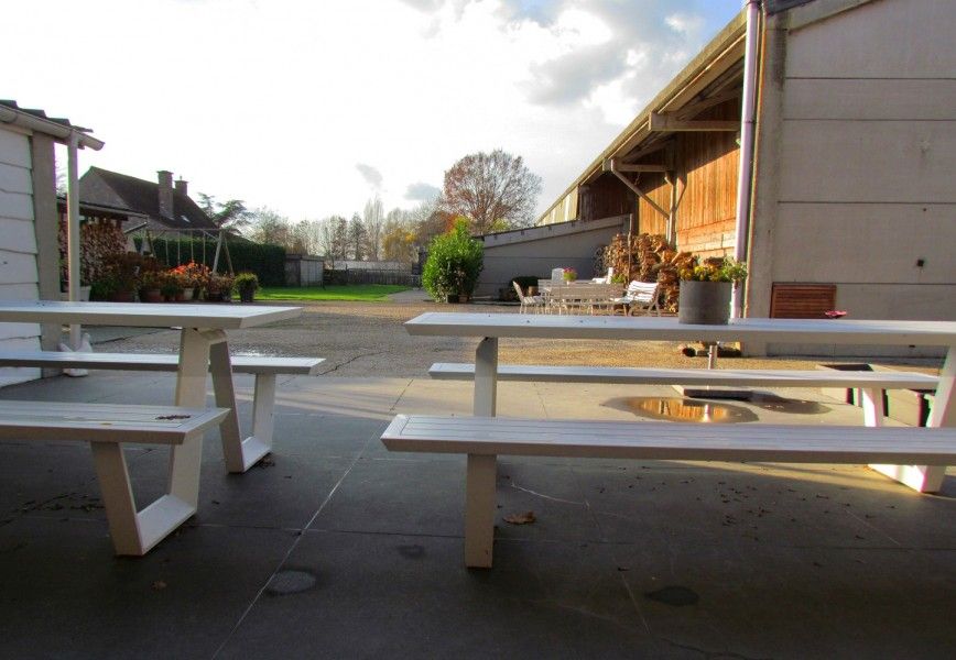 Blick auf den Innenhof des Ferienhauses Hof ter Harte, Ypern, Westflandern, mit Picknicktischen und blauem Himmel.