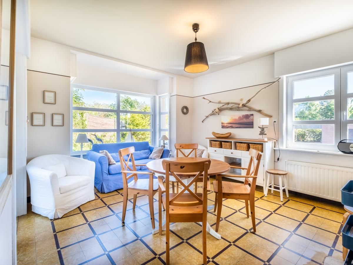 Gezellige woonkamer in Juvamy gelijkvloers, vakantiehuis in Koksijde, West-Vlaanderen, met veel lichtinval en uitzicht op de tuin.
