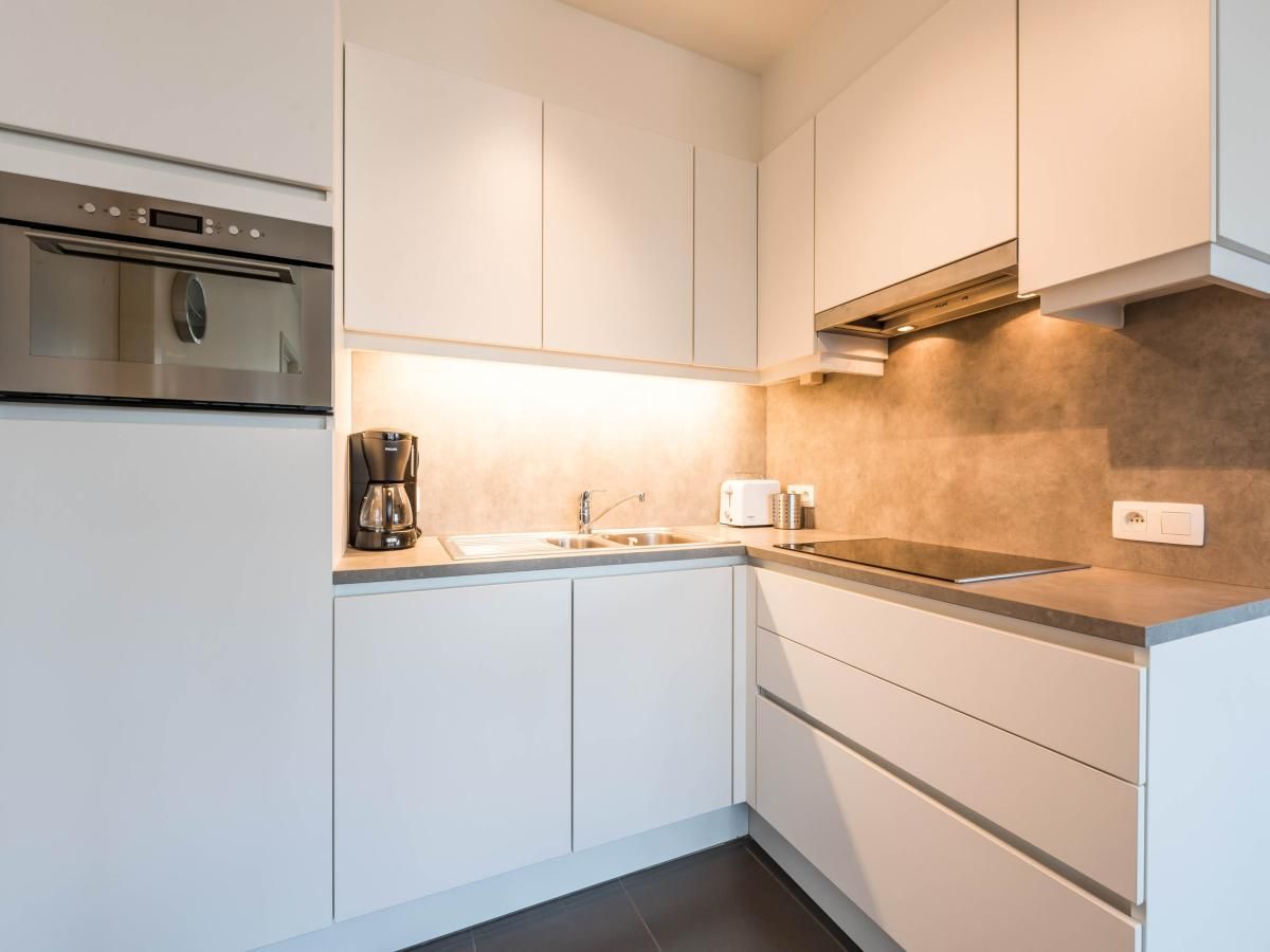 Moderne keuken in vakantiehuis De Dijk zesde, Koksijde, Belgie, met strakke witte kasten en ingebouwde apparatuur.