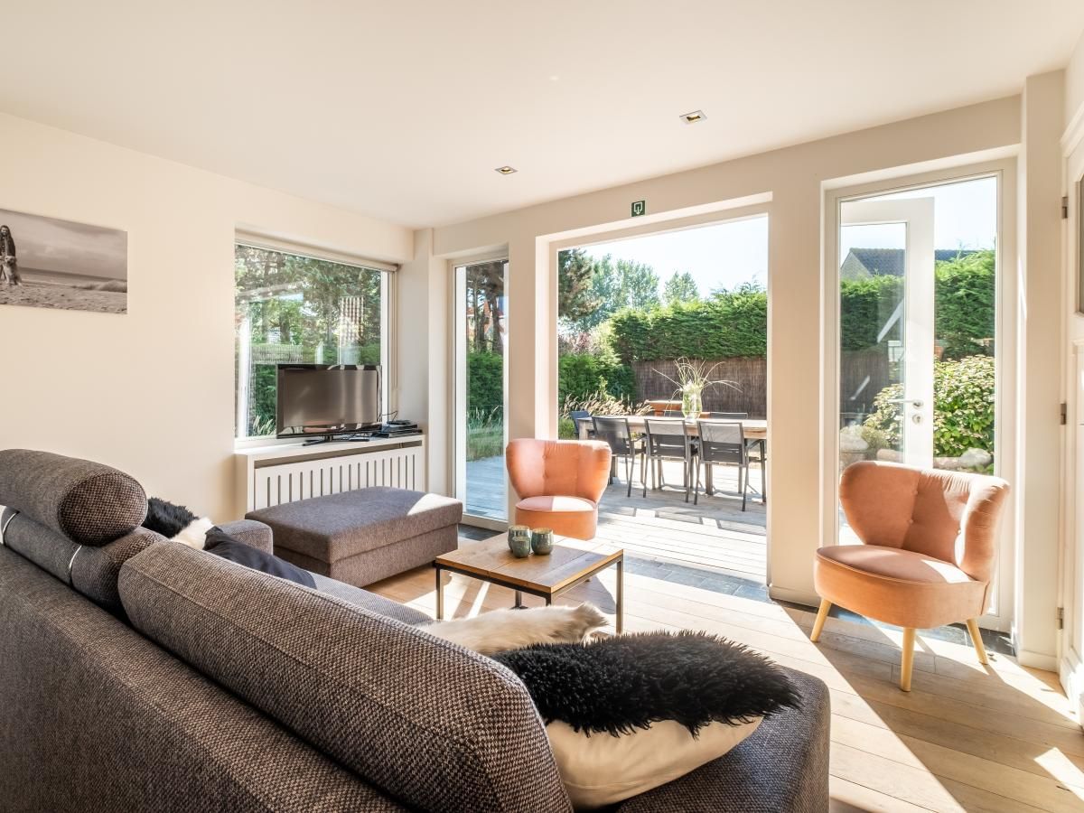 Lichte woonkamer van vakantiehuis Tranquil in Koksijde, West-Vlaanderen met uitzicht op zonnig terras en tuin.