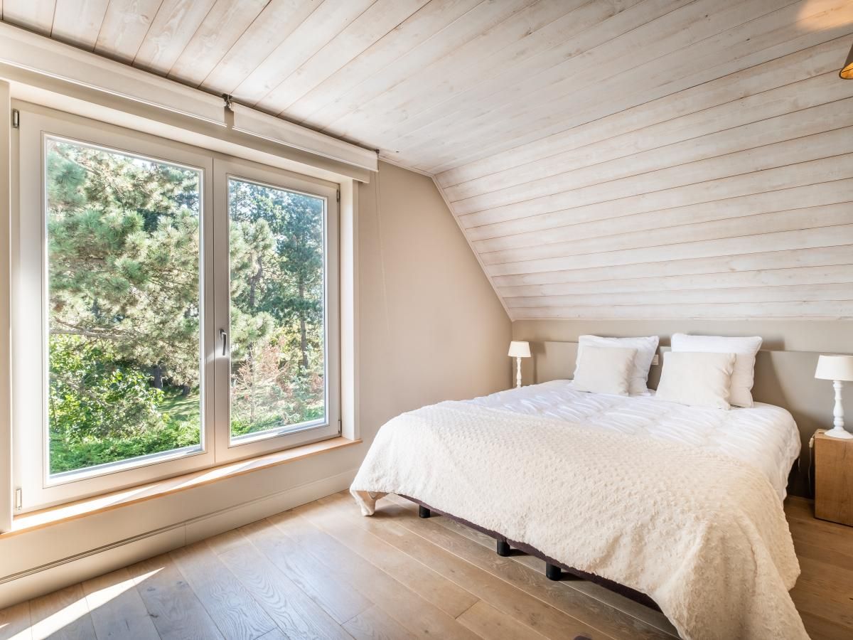 Slaapkamer in vakantiehuis Tranquil in Koksijde, West-Vlaanderen met uitzicht op groene natuur door grote ramen.