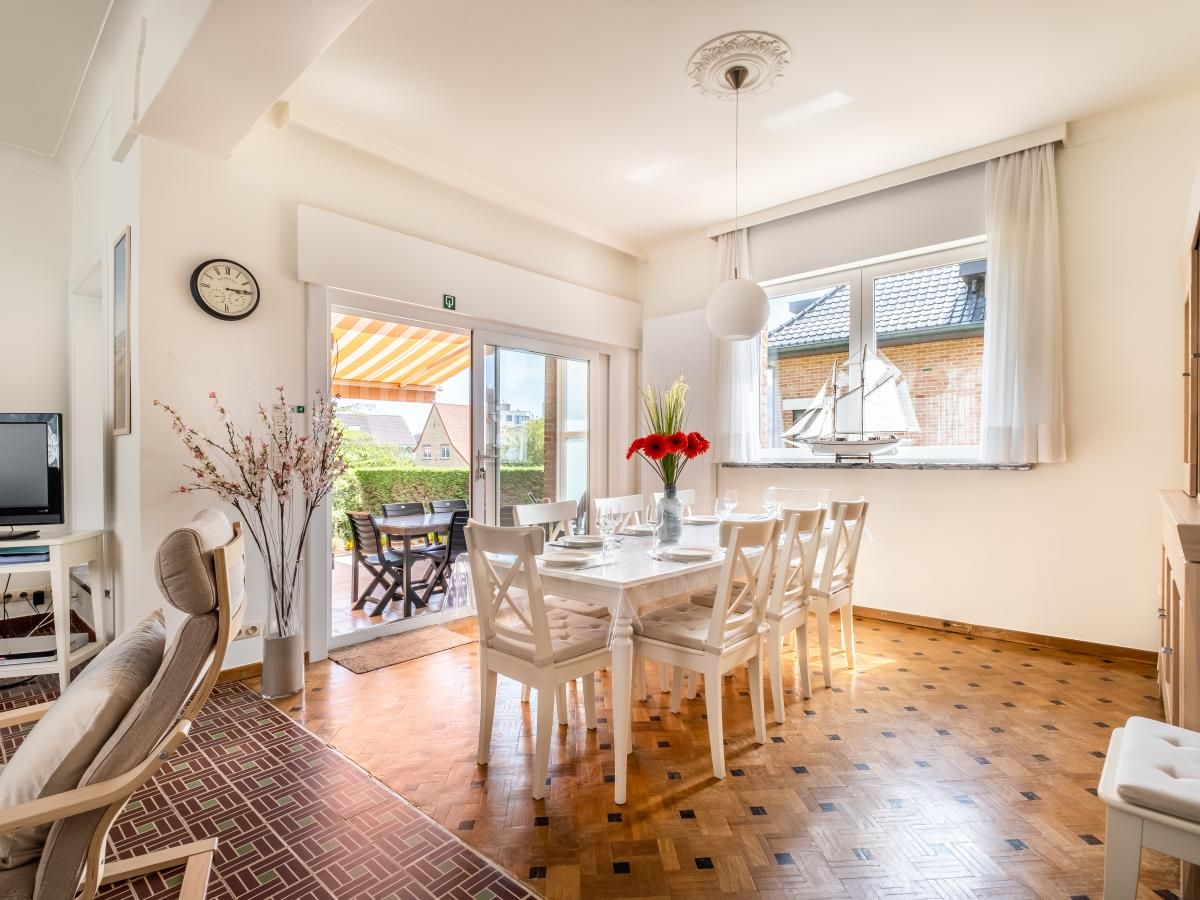 Lichte eetkamer in vakantiehuis Porpoises, Koksijde, met uitzicht op zonnig terras en tuin, ideaal voor een ontspannen verblijf in West-Vlaanderen.