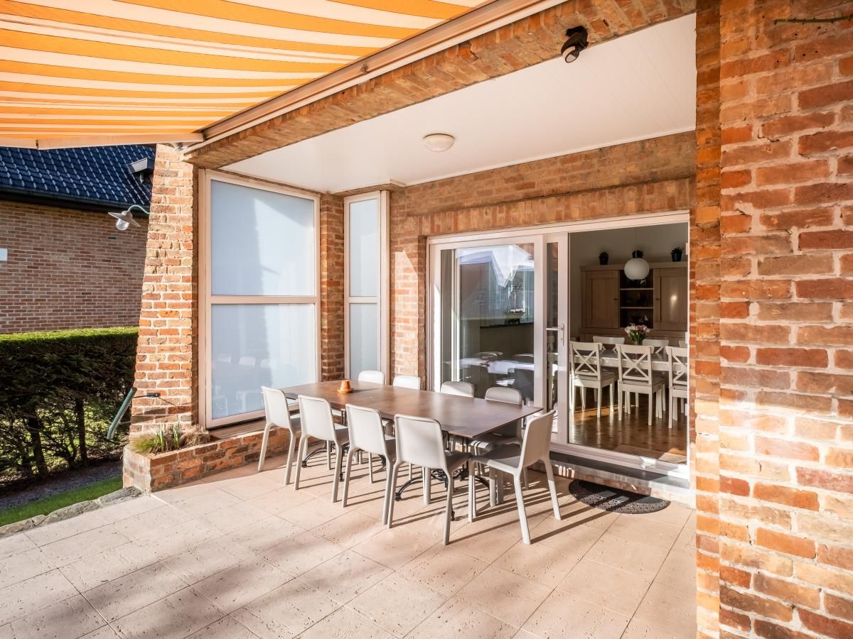 Gezellige veranda bij vakantiehuis Porpoises in Koksijde, West-Vlaanderen, perfect voor buiten dineren en ontspannen in de zon.