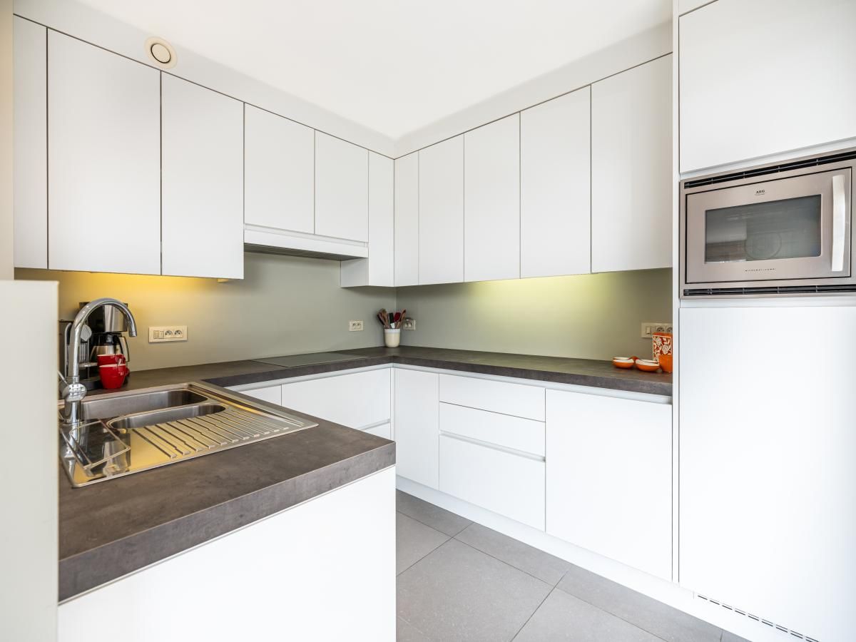 Moderne keuken in Tinou Gelijkvloers vakantiehuis in Koksijde, West-Vlaanderen, met strakke witte kasten en ruime werkbladen.