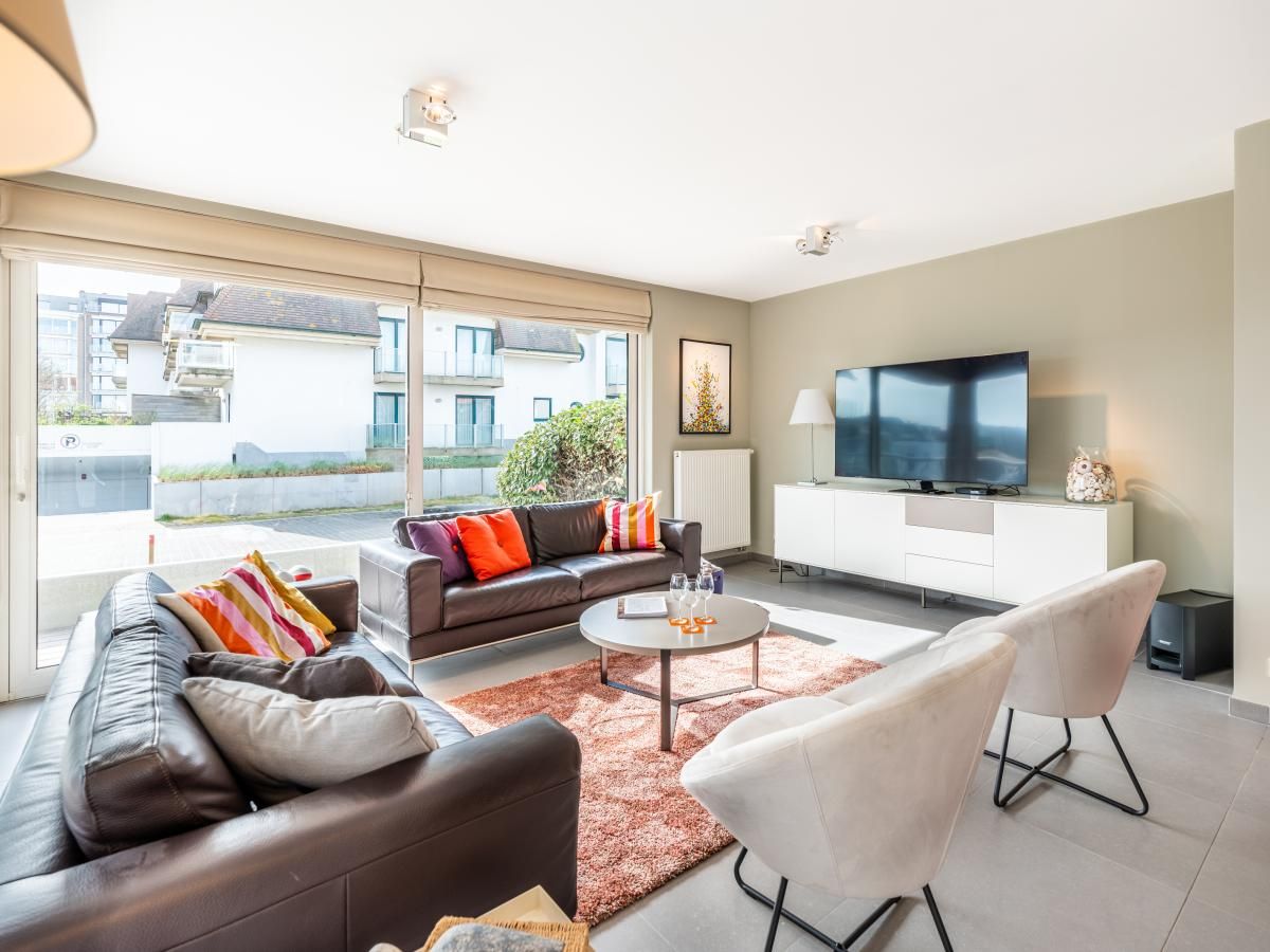 Gezellige woonkamer in Tinou Gelijkvloers, vakantiehuis in Koksijde, West-Vlaanderen. Comfortabele zithoek met veel natuurlijk licht.