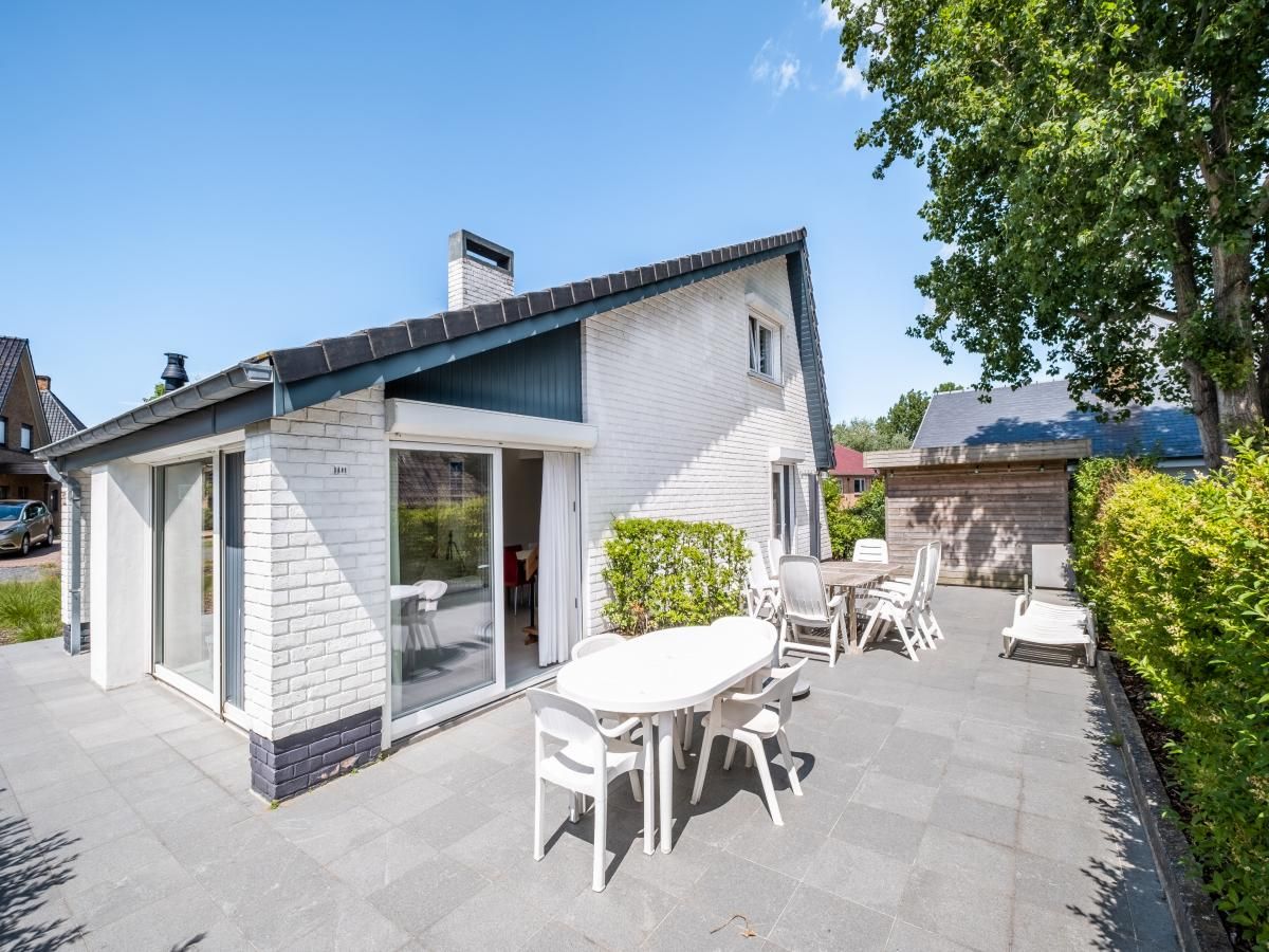 Ruim terras bij vakantiehuis Guillaume in Koksijde, West-Vlaanderen, Belgie, omgeven door groen en voorzien van comfortabele zitgelegenheden.