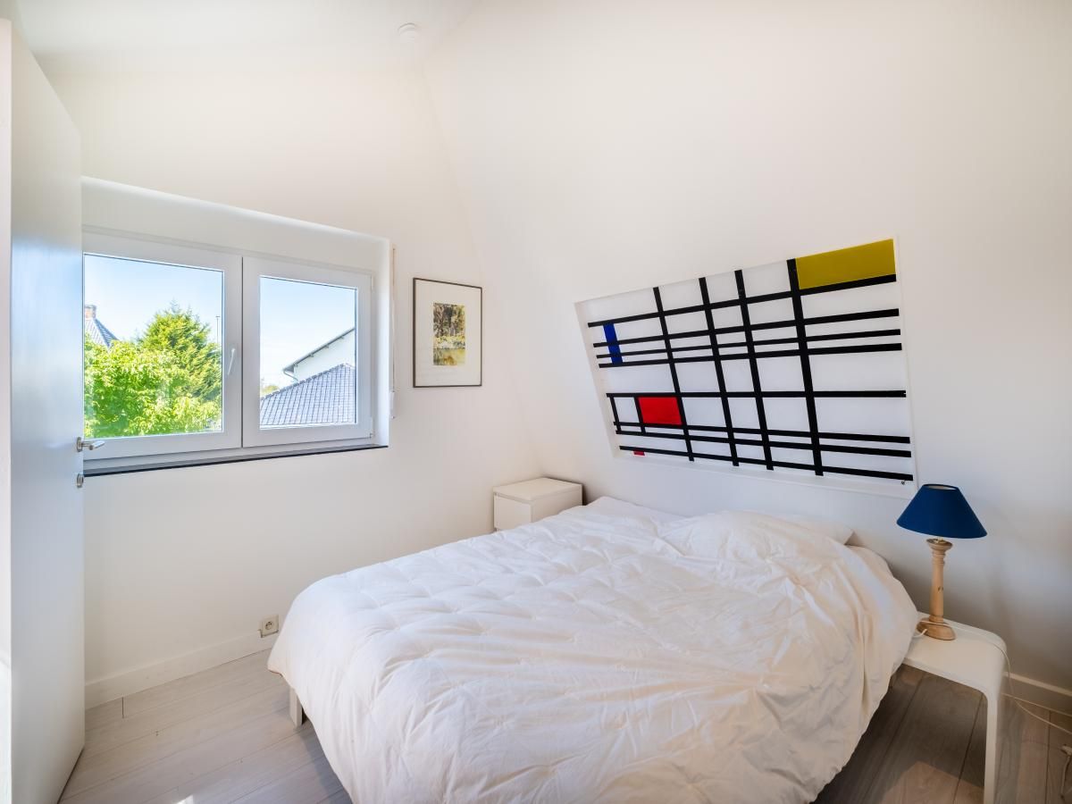 Sfeervolle slaapkamer van vakantiehuis Guillaume in Koksijde, West-Vlaanderen, Belgie, met modern kunstwerk en uitzicht op groene omgeving.