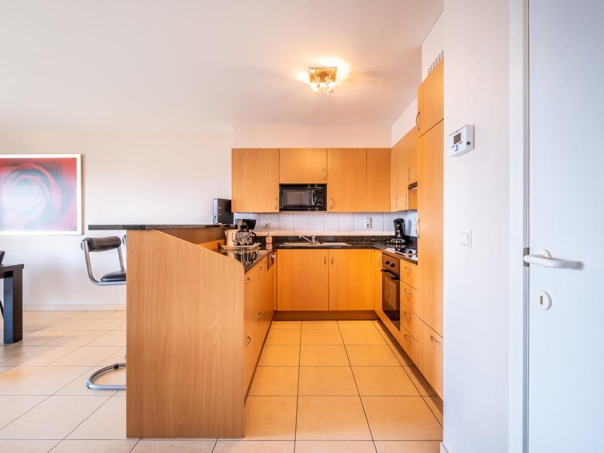 Moderne keuken in vakantiehuis Paco vierde, Koksijde, West-Vlaanderen. Ruime binnenruimte met houten kasten en tegelvloer.