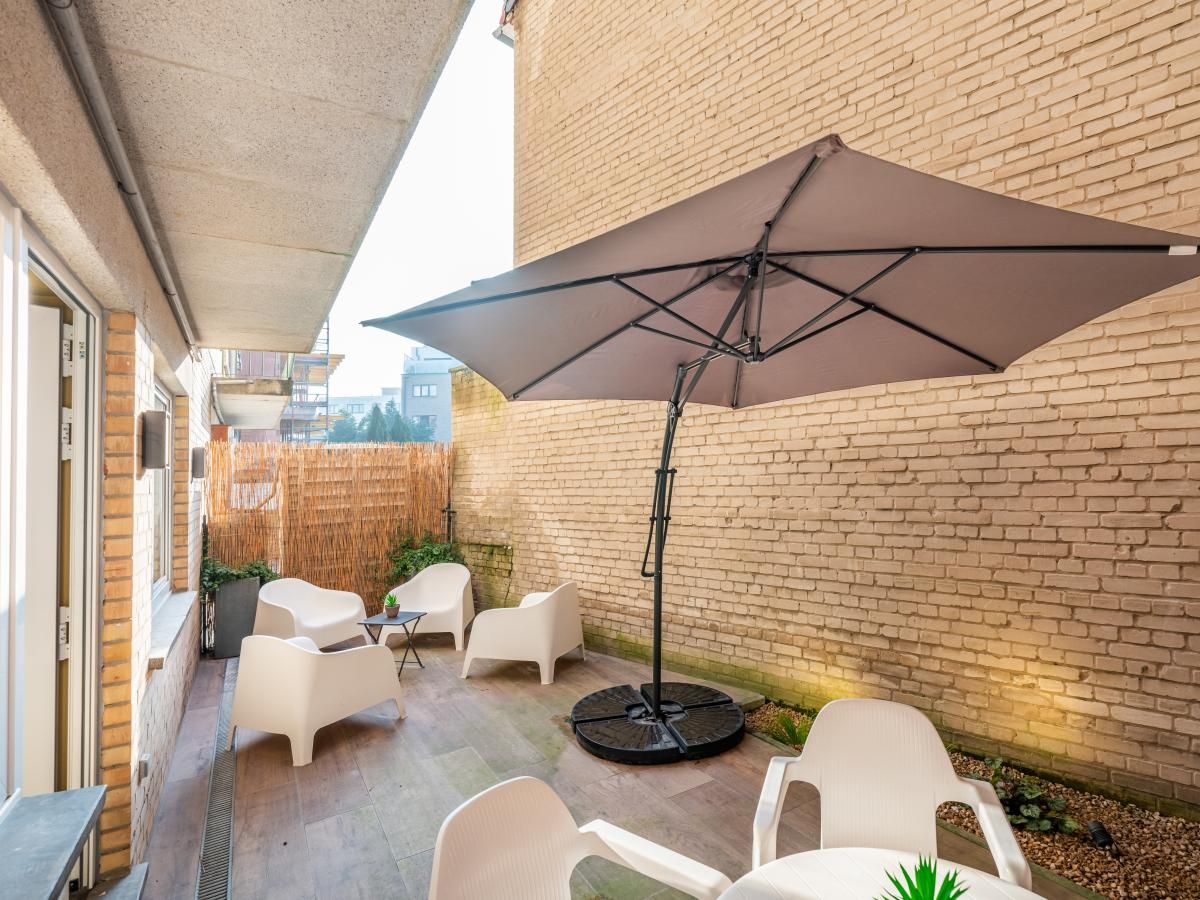 Ontspan op het terras van vakantiehuis Bon Plan in Koksijde, West-Vlaanderen, met moderne zitjes en een grote parasol voor schaduw.