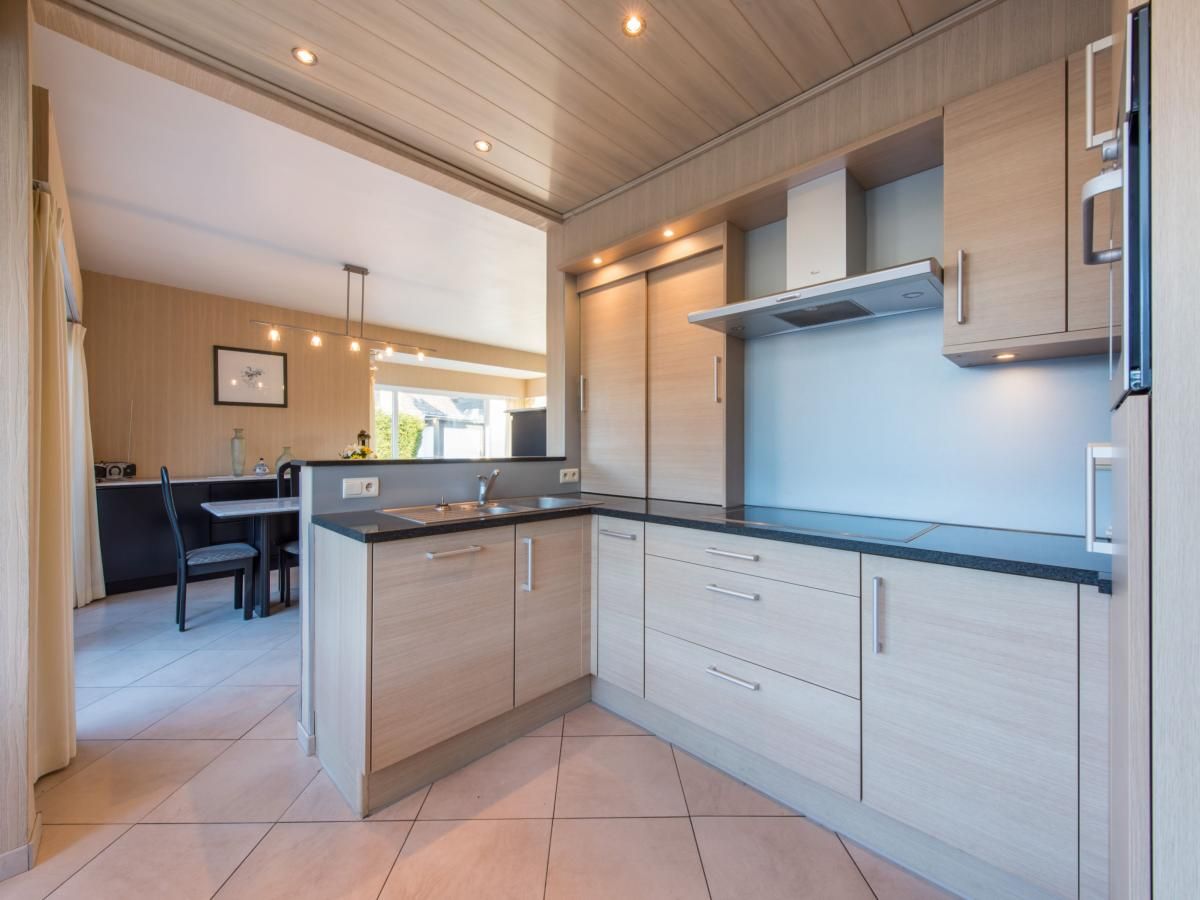Moderne keuken in vakantiehuis Mallory in Koksijde, West-Vlaanderen, met houten kasten en ruime eetkamer, ideaal voor een ontspannen verblijf.
