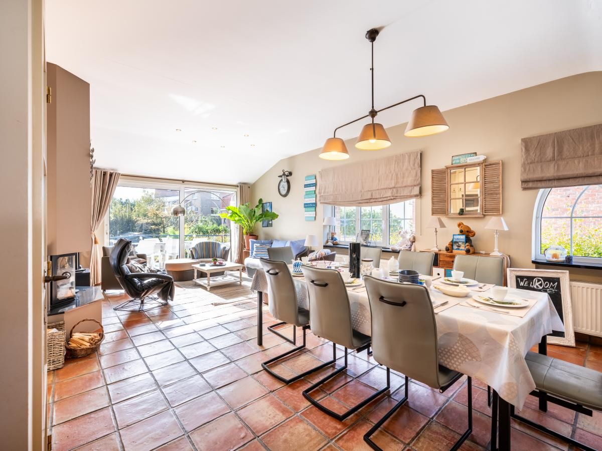 Gezellige woonkamer van vakantiehuis Le Palmier in Koksijde, West-Vlaanderen, met eethoek en uitzicht op de tuin.