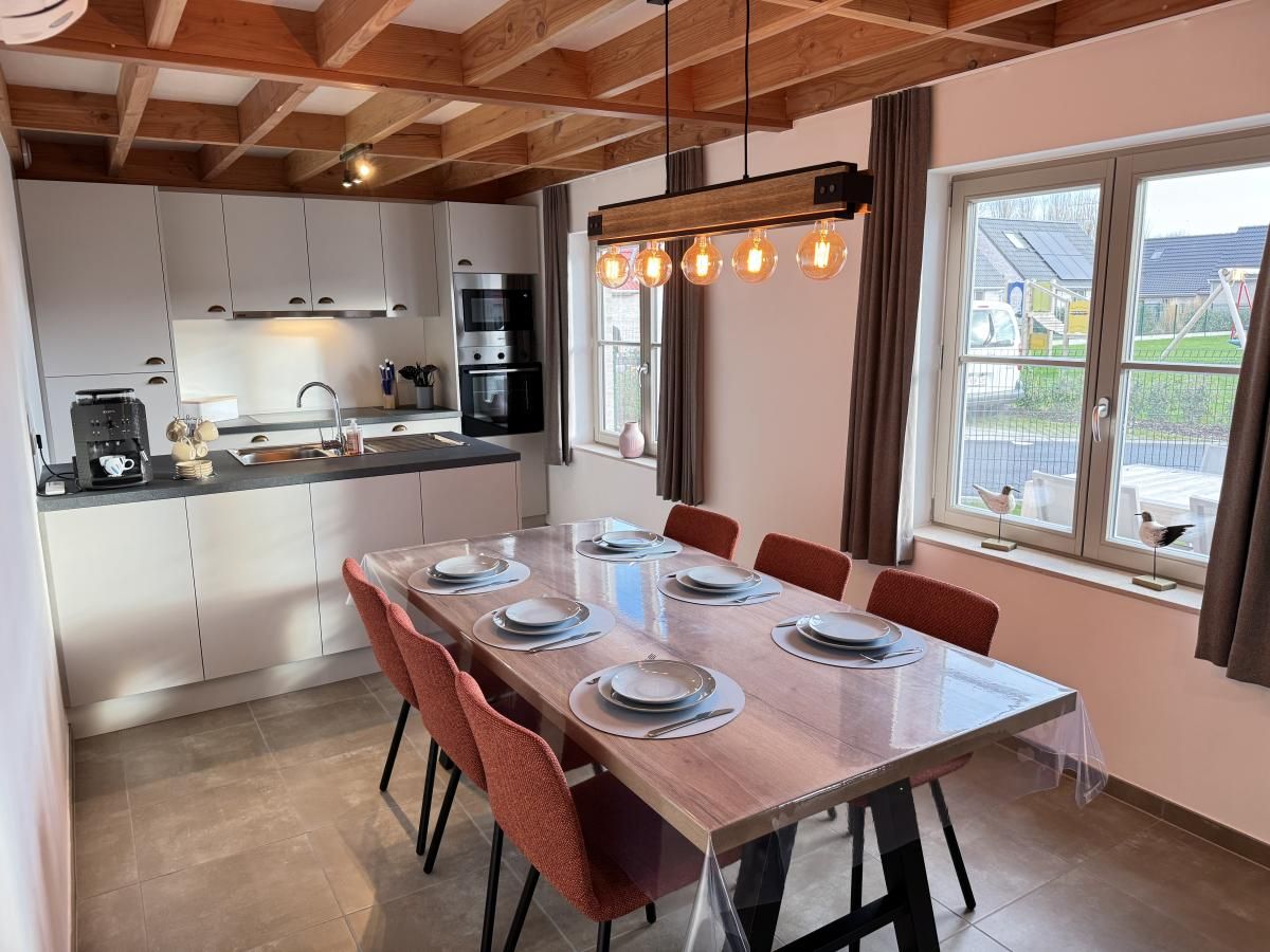 Gezellige eetkamer en keuken in vakantiehuis Westhinder II H23, Koksijde, West-Vlaanderen, met moderne inrichting en uitzicht op de tuin.