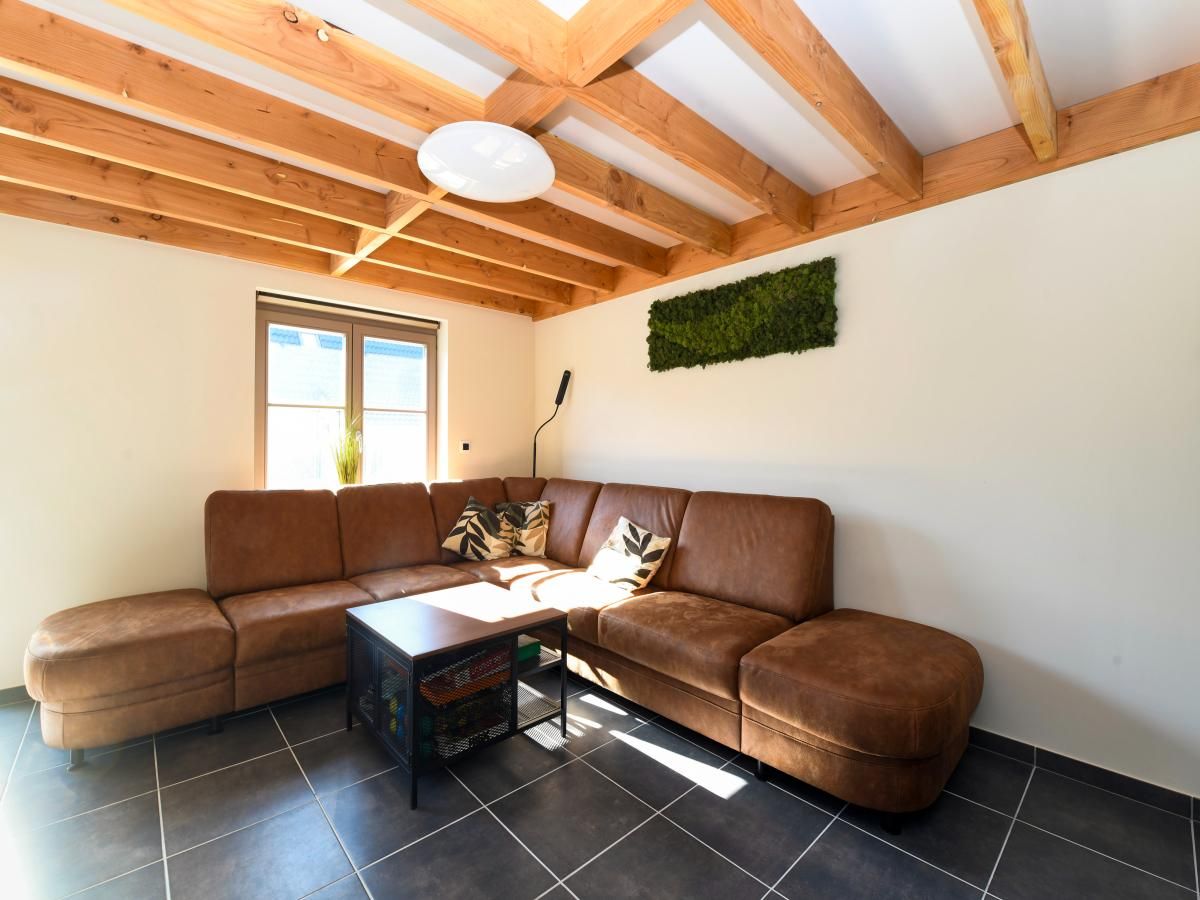 Gemuetliches Wohnzimmer des Ferienhauses Westhinder II H53 in Koksijde, Westflandern, mit bequemer Sitzecke und Holzbalkendecke.