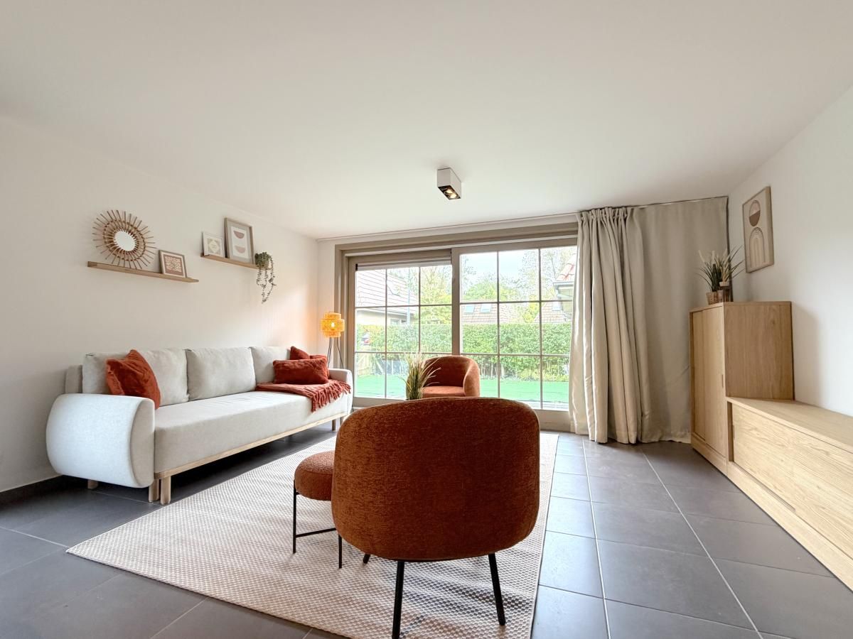 Gemuetliches Wohnzimmer im Ferienhaus Home Sweet Home, De Panne, mit moderner Einrichtung und Blick auf den gruenen Garten in Westflandern, Belgien.