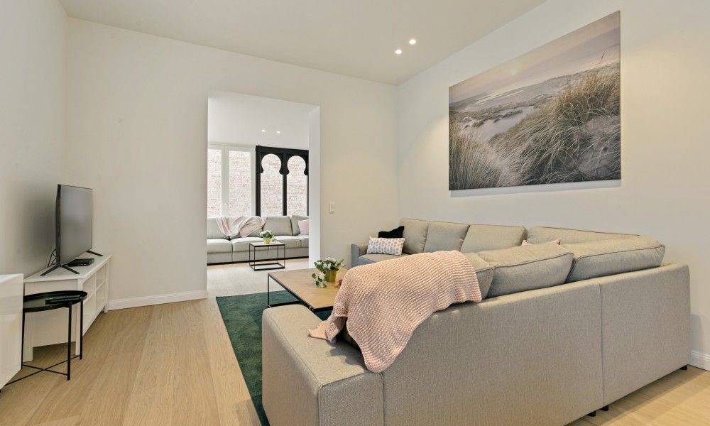 Gemuetliches Wohnzimmer von Maison Perron, Ferienhaus De Panne, Westflandern mit bequemem Sofa und Kunst an der Wand.