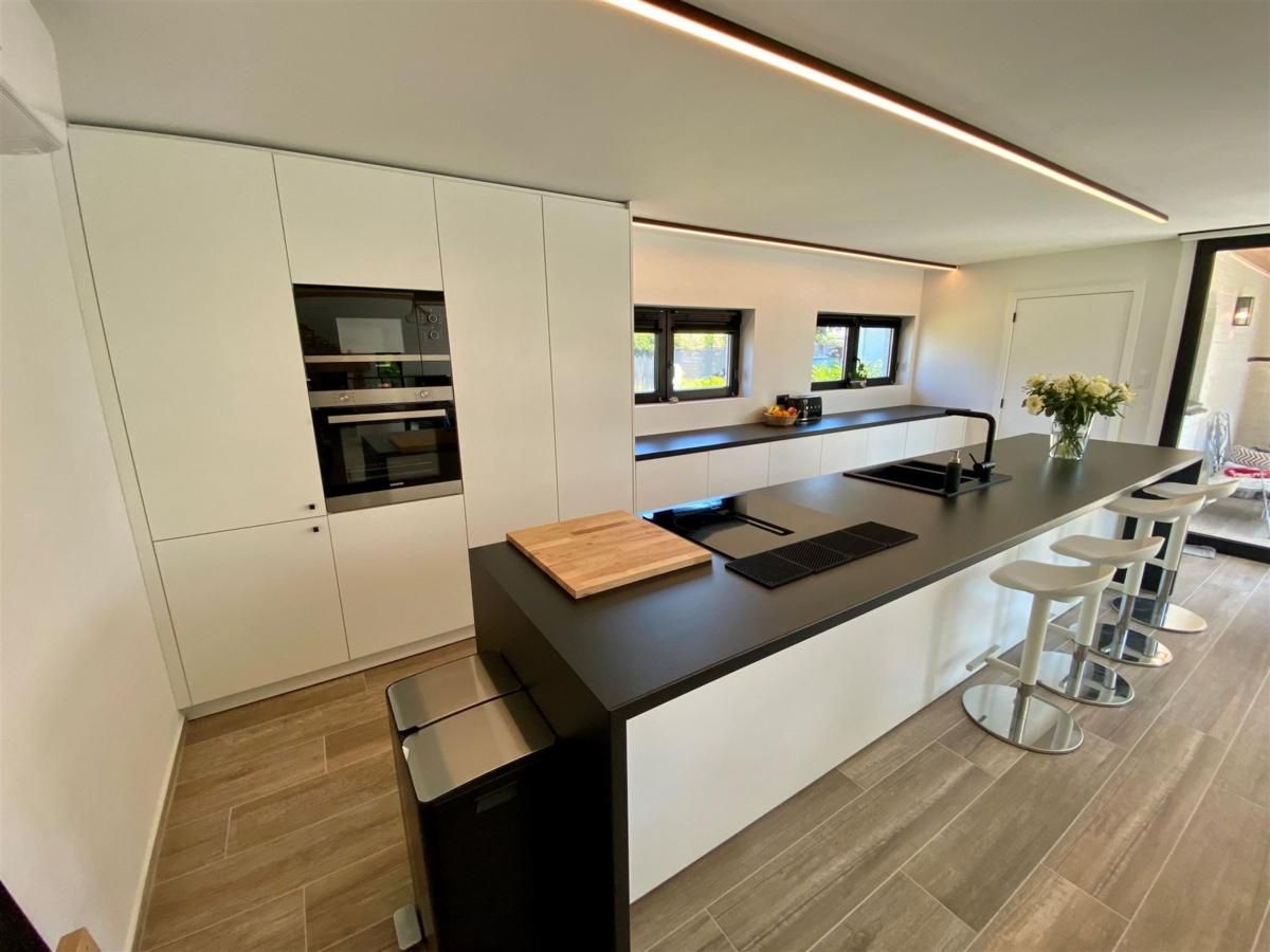 Moderne Kueche im Ferienhaus Petunias Deluxe, Sint-Idesbald, Westflandern. Luxurioeses Interieur mit Insel und glatter Oberflaeche.