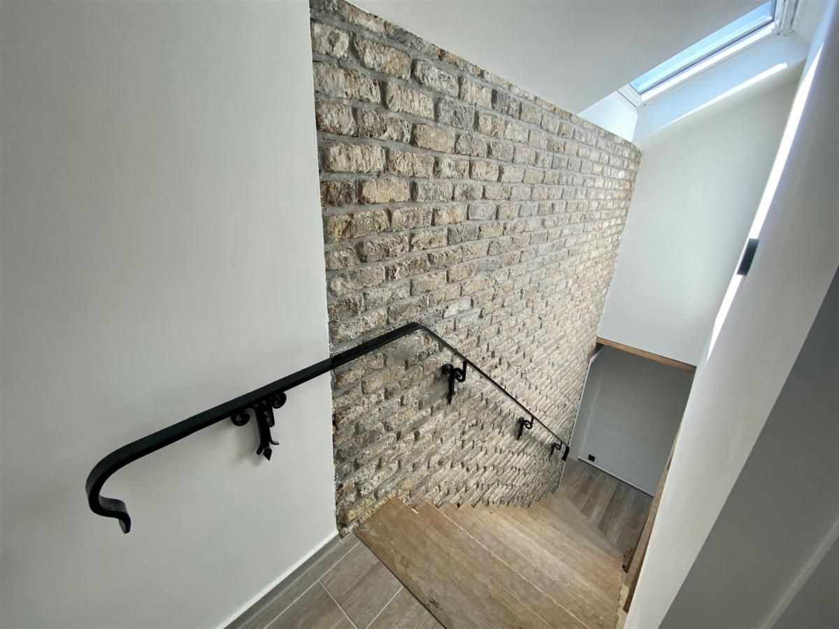 Stilvolles Treppenhaus im Ferienhaus Petunias Deluxe, Sint-Idesbald, Belgien, mit rustikaler Ziegelwand und modernen Oberflaechen.