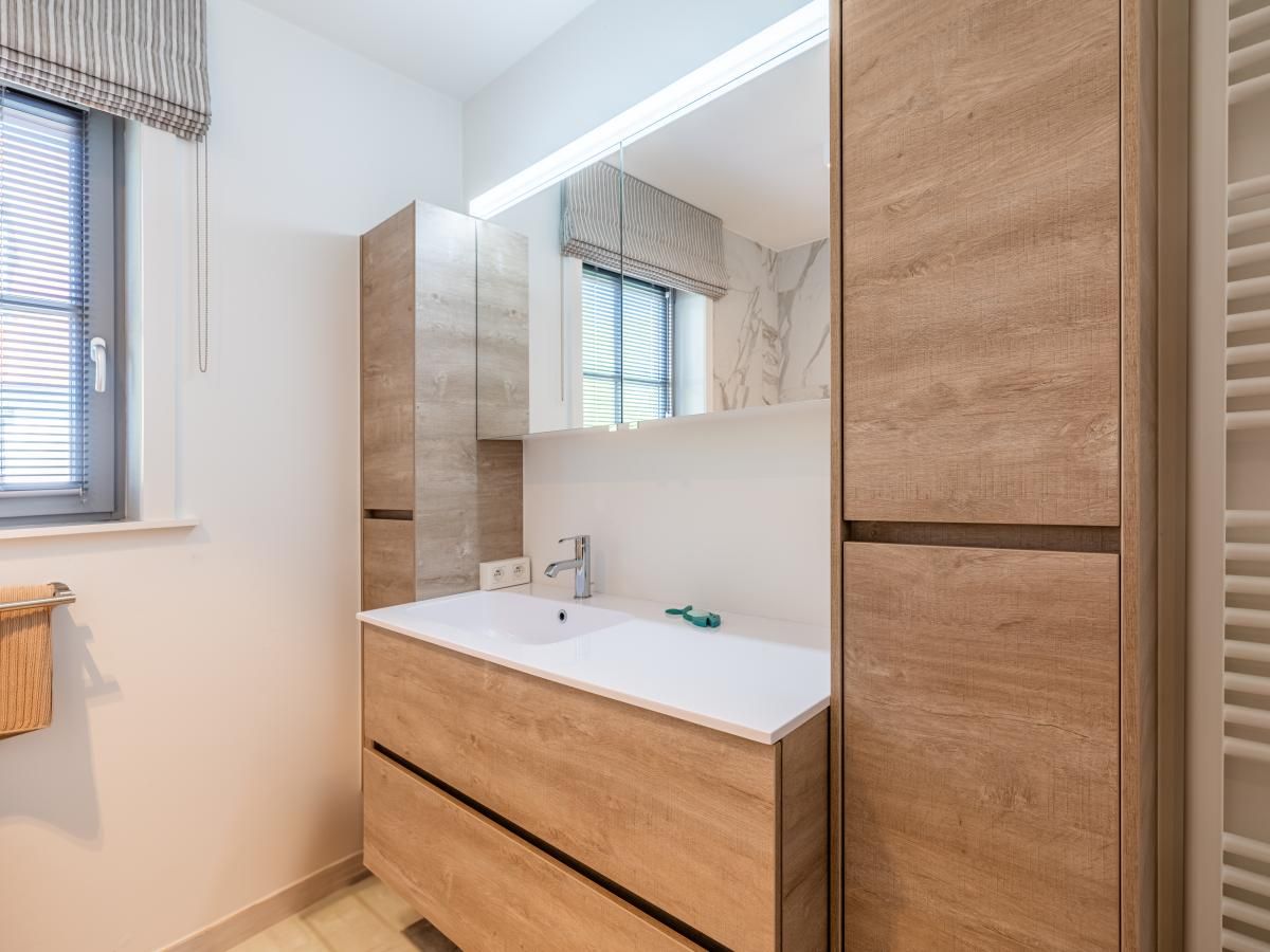 Moderne badkamer in La Matinee vakantiehuis, Sint-Idesbald, West-Vlaanderen, met houten meubels en natuurlijk licht.