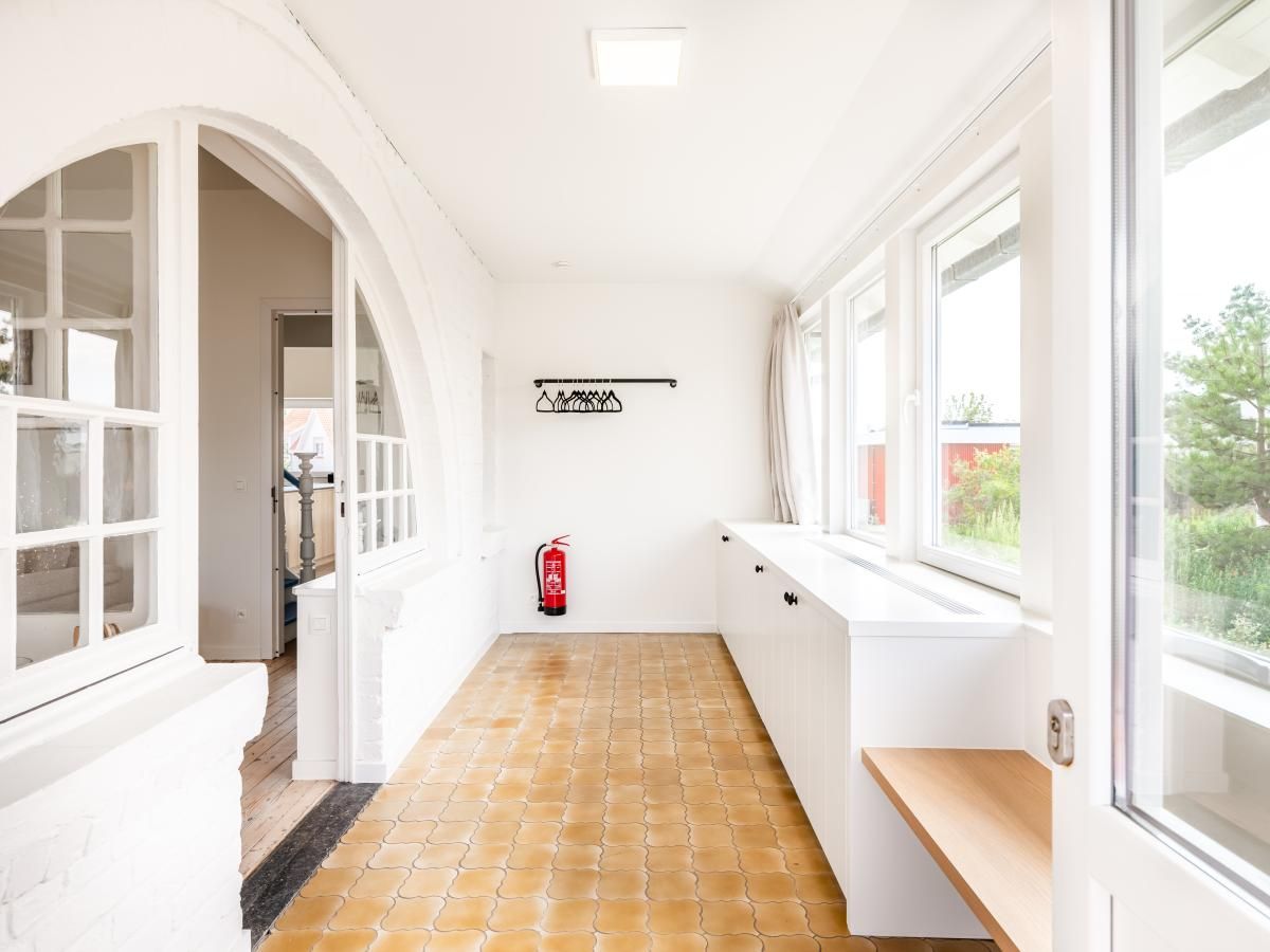 Lichte binnenruimte van vakantiehuis La Classe in Sint-Idesbald, West-Vlaanderen, met grote ramen en rustieke tegelvloer.