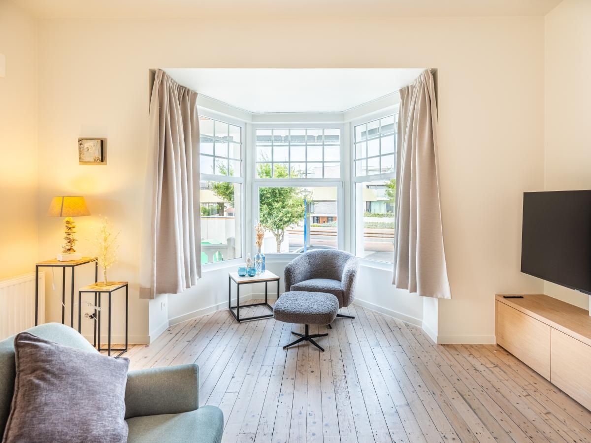 Lichte woonkamer in vakantiehuis La Classe, Sint-Idesbald, met stijlvolle inrichting en uitzicht op de tuin in West-Vlaanderen, Belgie.