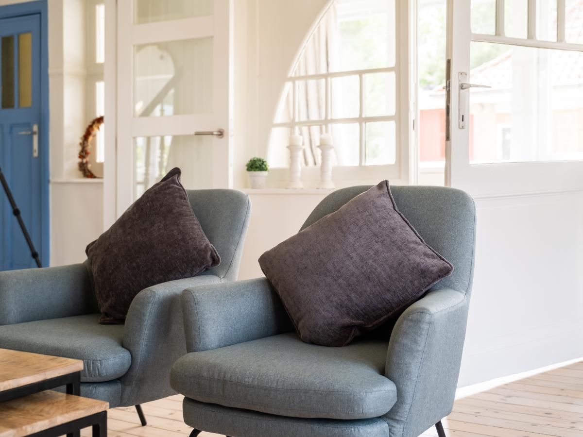 Lichte woonkamer van vakantiehuis La Classe in Sint-Idesbald, West-Vlaanderen, met comfortabele stoelen en grote ramen.
