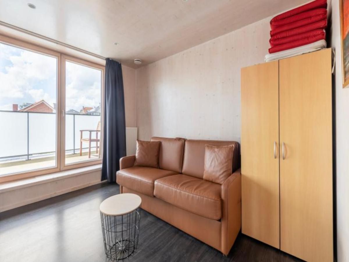 Gemuetlicher Innenbereich der Kruiers Eco Lodge in Middelkerke, Belgien, mit bequemem Sofa und grossem Fenster fuer natuerliches Licht.