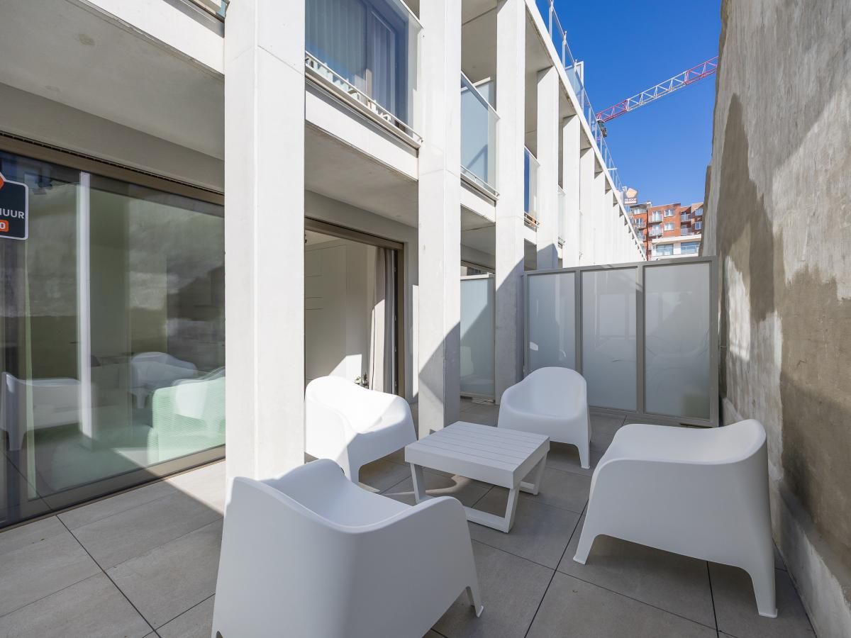 Moderne Veranda des Ferienhauses Omnia 7 - 0103 + Park. 5 in Middelkerke, Westflandern, Belgien, mit weissen Stuehlen und einem kleinen Tisch.