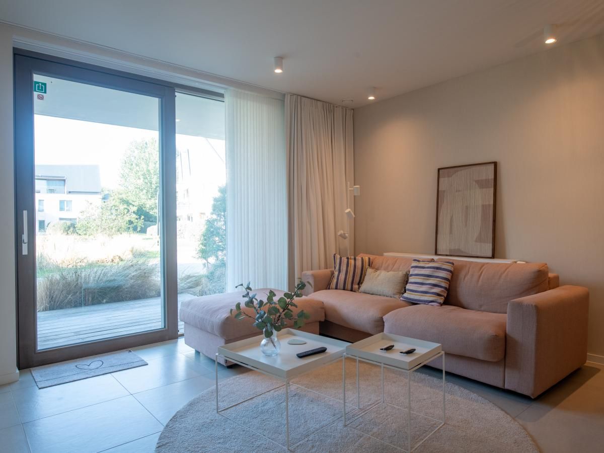 Gezellige woonkamer van West Bay vakantiehuis in Westende, West-Vlaanderen met comfortabele bank en uitzicht op de tuin.