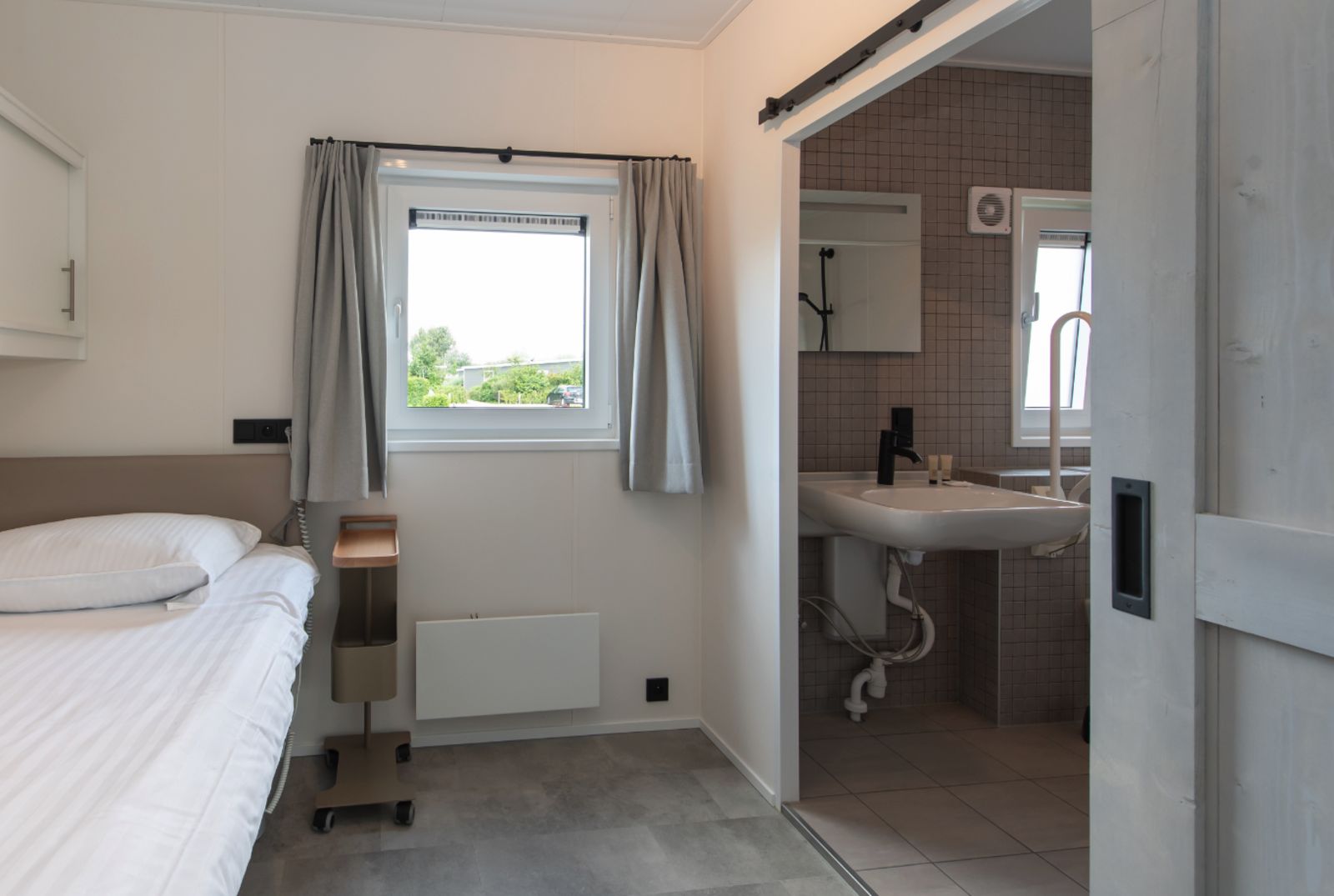 Modernes Schlafzimmer und Badezimmer in Access Lodge, einem Ferienhaus in Westende, Westflandern, mit Blick auf die gruene Umgebung.