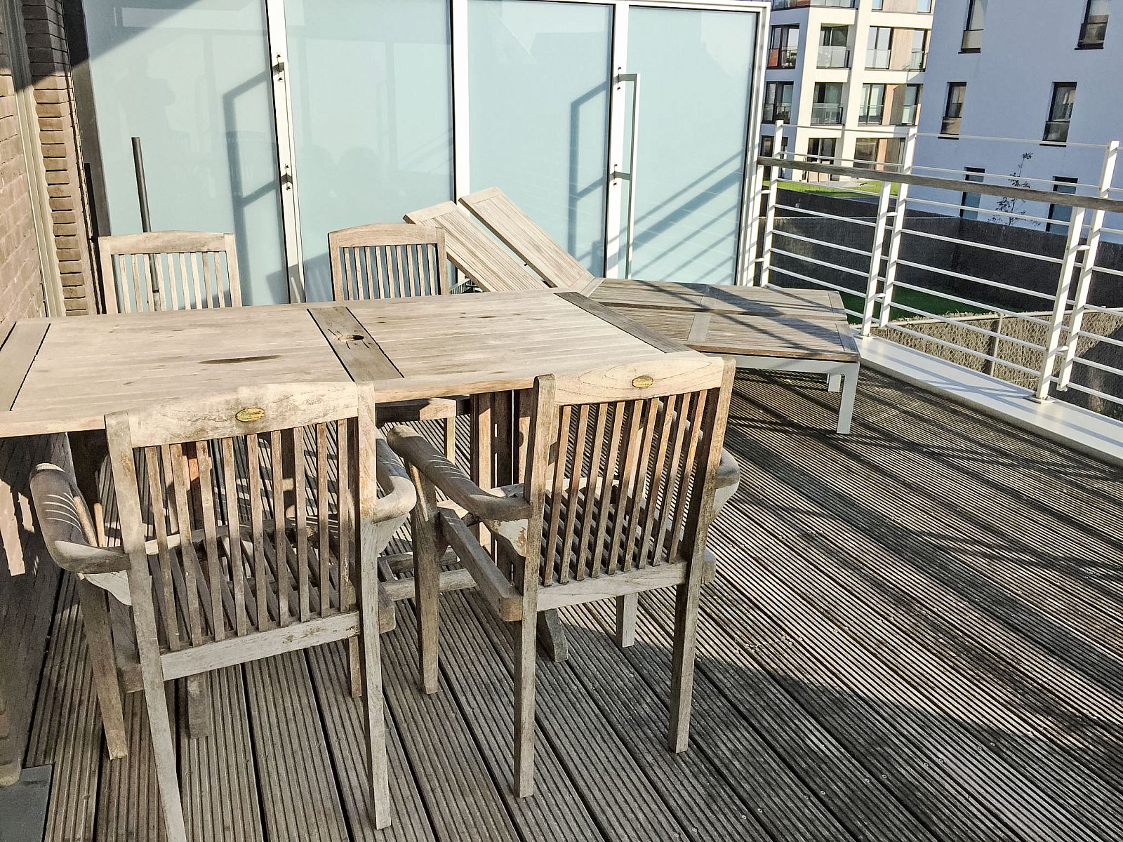 Zonnig terras van Appartement Cocoon in Bredene, West-Vlaanderen, Belgie, met houten tuinmeubilair en uitzicht op de moderne omgeving.