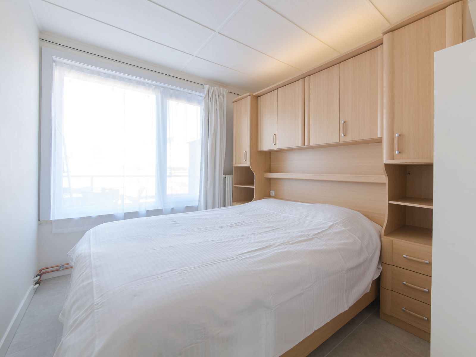 Schlafzimmer des Apartments Casa Bunck in Bredene, Westflandern, mit einem bequemen Doppelbett und natuerlichem Licht durch grosse Fenster.