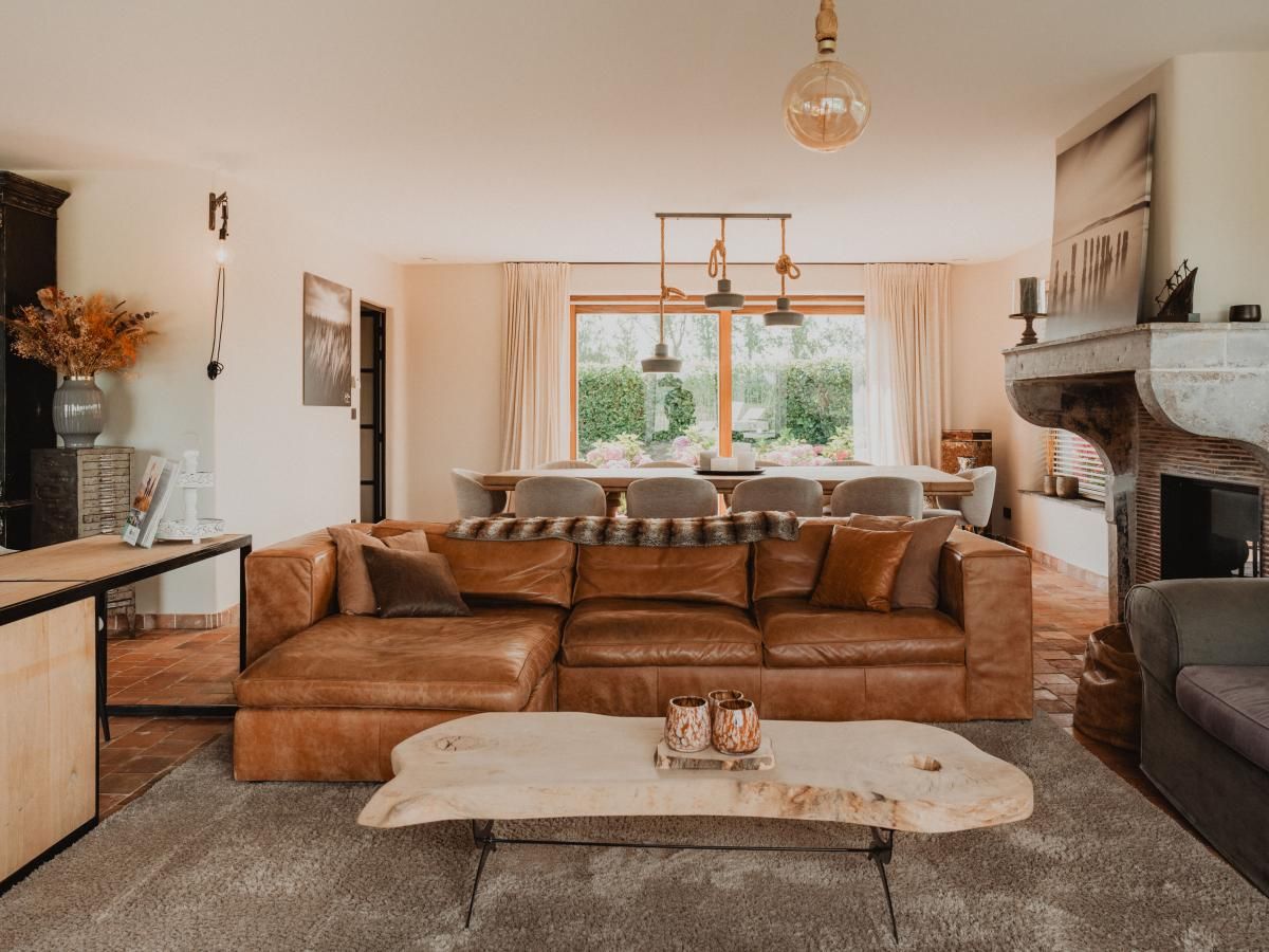 Stijlvolle woonkamer van Villa Noortem, een vakantiehuis in Maldegem, Oost-Vlaanderen, met luxe leren bank en sfeervolle open haard.