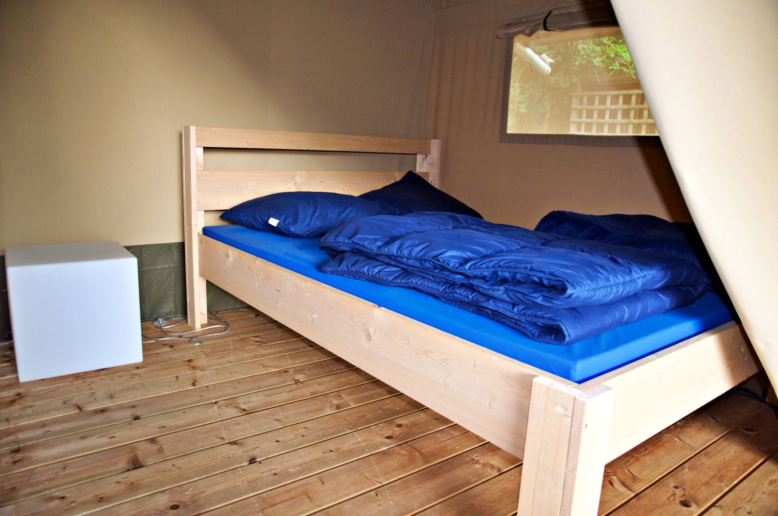Gemuetliches Schlafzimmer im Safari-Zelt, einer Glamping-Lodge in Brecht, Antwerpen, Belgien, mit bequemem Holzbett und natuerlichem Licht.