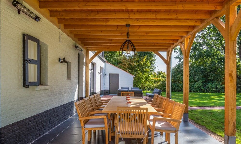 Ueberdachte Terrasse des Ferienhauses Mushoeve in Zoersel, Antwerpen, mit Esstisch aus Holz und Gartenblick.