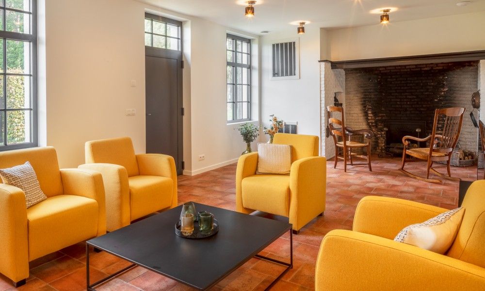 Gemuetliches Wohnzimmer von Mushoeve in Zoersel, Antwerpen mit Kamin und bequemen gelben Stuehlen.