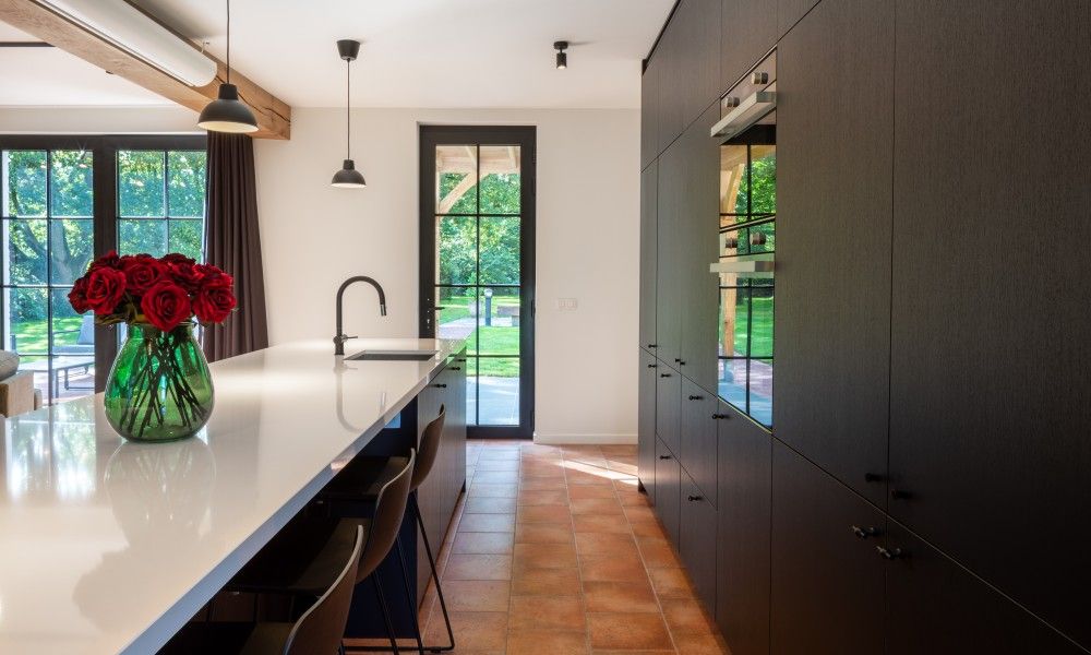 Moderne Kueche des Ferienhauses Mushoeve in Zoersel, Antwerpen mit Insel und Blick auf die gruene Umgebung.