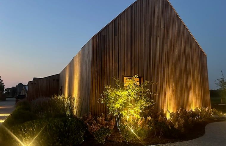 Ferienhaus in Kasterlee, Antwerpen, Belgien, attraktiv beleuchtet in der Abenddaemmerung mit Holzfassade und umgebender Natur.