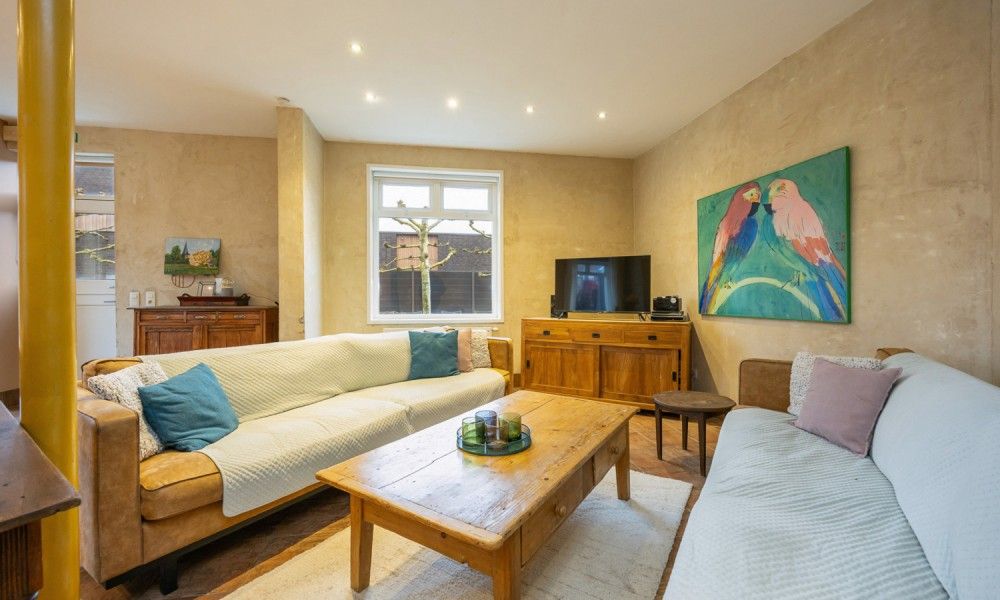Gezellige woonkamer van vakantiehuis De Morgenstond in Baarle-Hertog, Antwerpen, met comfortabele banken en kleurrijke kunst aan de muur.
