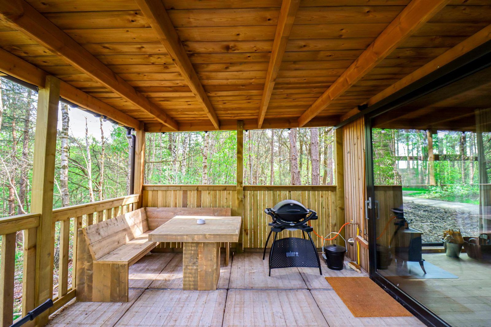 Overdekte veranda van Comfort Classic in Neeroeteren, Limburg, Belgie, met houten zitgedeelte en barbecue, omgeven door natuur.