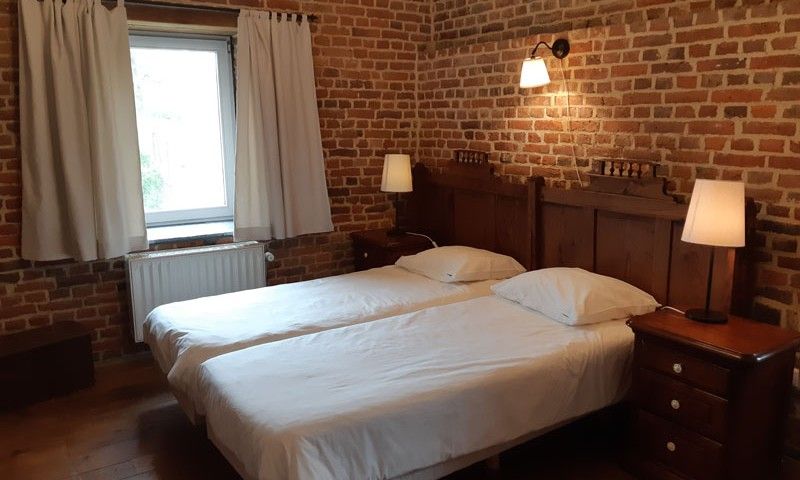 Gezellige slaapkamer in Servaeshoeve - Gerstebaard, vakantiehuis in Borgloon, Limburg, Belgie, met rustieke bakstenen muren en houten meubels.