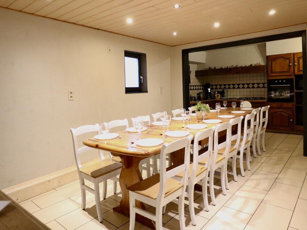 Ruime eetkamer van vakantiehuis Annexe in Sourbrodt, Ardennen, Belgie met lange houten tafel en moderne keuken in de achtergrond.