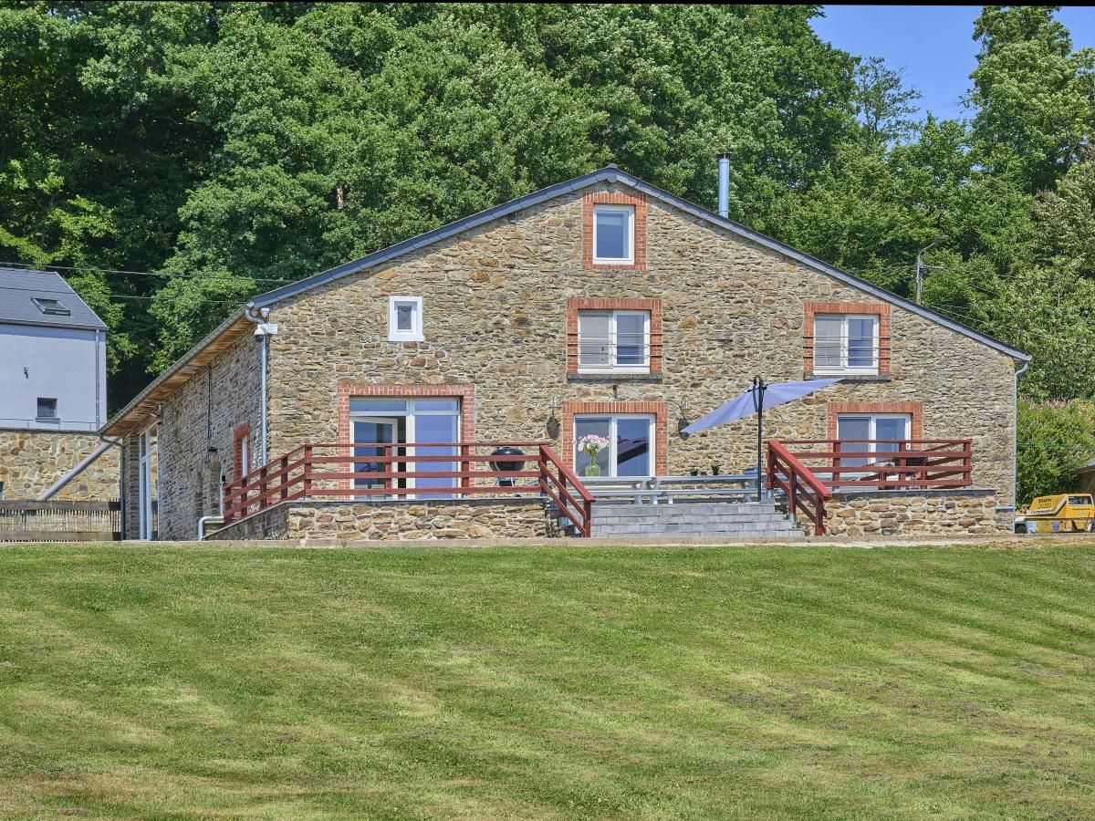 Das Ferienhaus "La Ferme" in Lierneux, Ardennen, Belgien, mit rustikaler Steinfassade und einer grosszuegigen Terrasse, umgeben von gruener Natur.