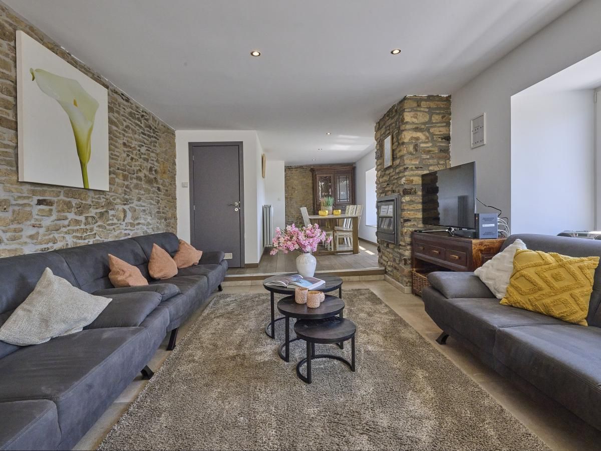 Gemuetliches Wohnzimmer im Ferienhaus "La Ferme" in Lierneux, Ardennen, mit bequemen Sofas und rustikalen Steinwaenden in Belgien.