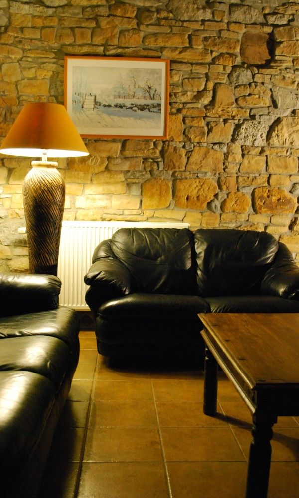 Gezellige zithoek met leren banken in Gites d'Ogne vakantiehuis in Sprimont-Ogne, Ardennen, met sfeervolle stenen muur.