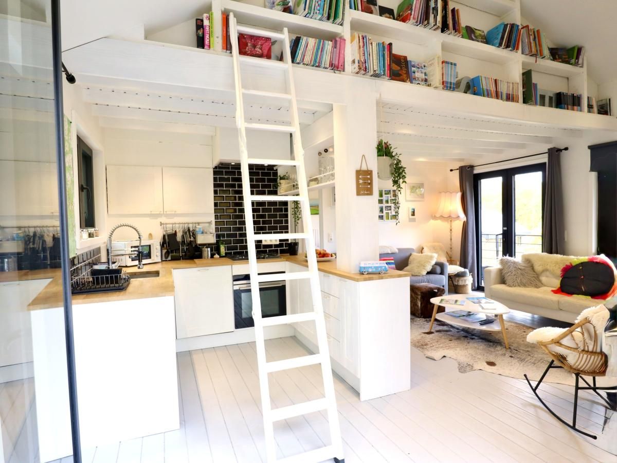 Interior space of chalet Agathe in Laforet, Ardennes, with cozy sitting area and modern kitchen, surrounded by books and natural light.