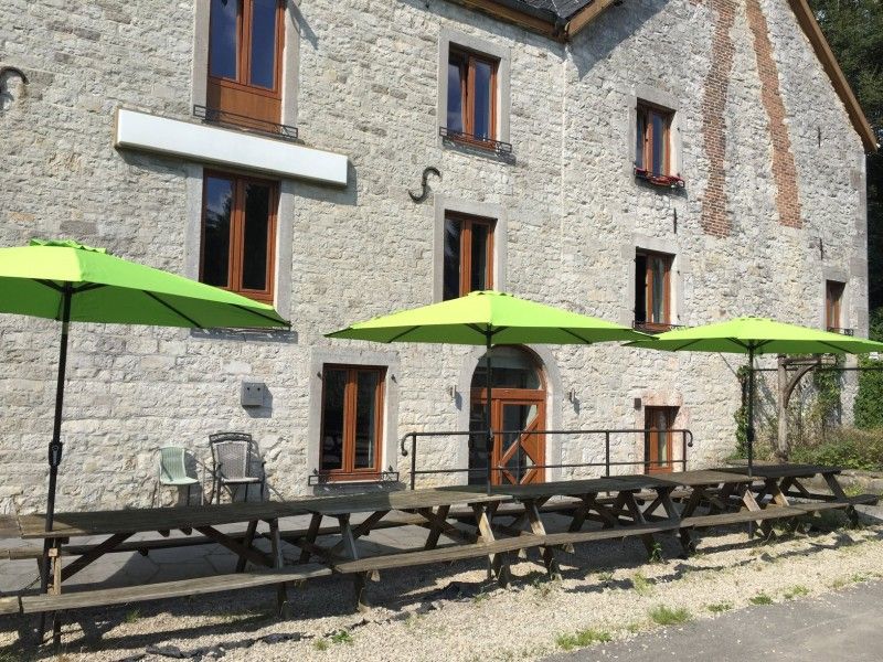 Terrasse von Le Moulin De Romedenne in Philippeville, Ferienhaus in den Ardennen mit gruenen Sonnenschirmen und Holztischen.