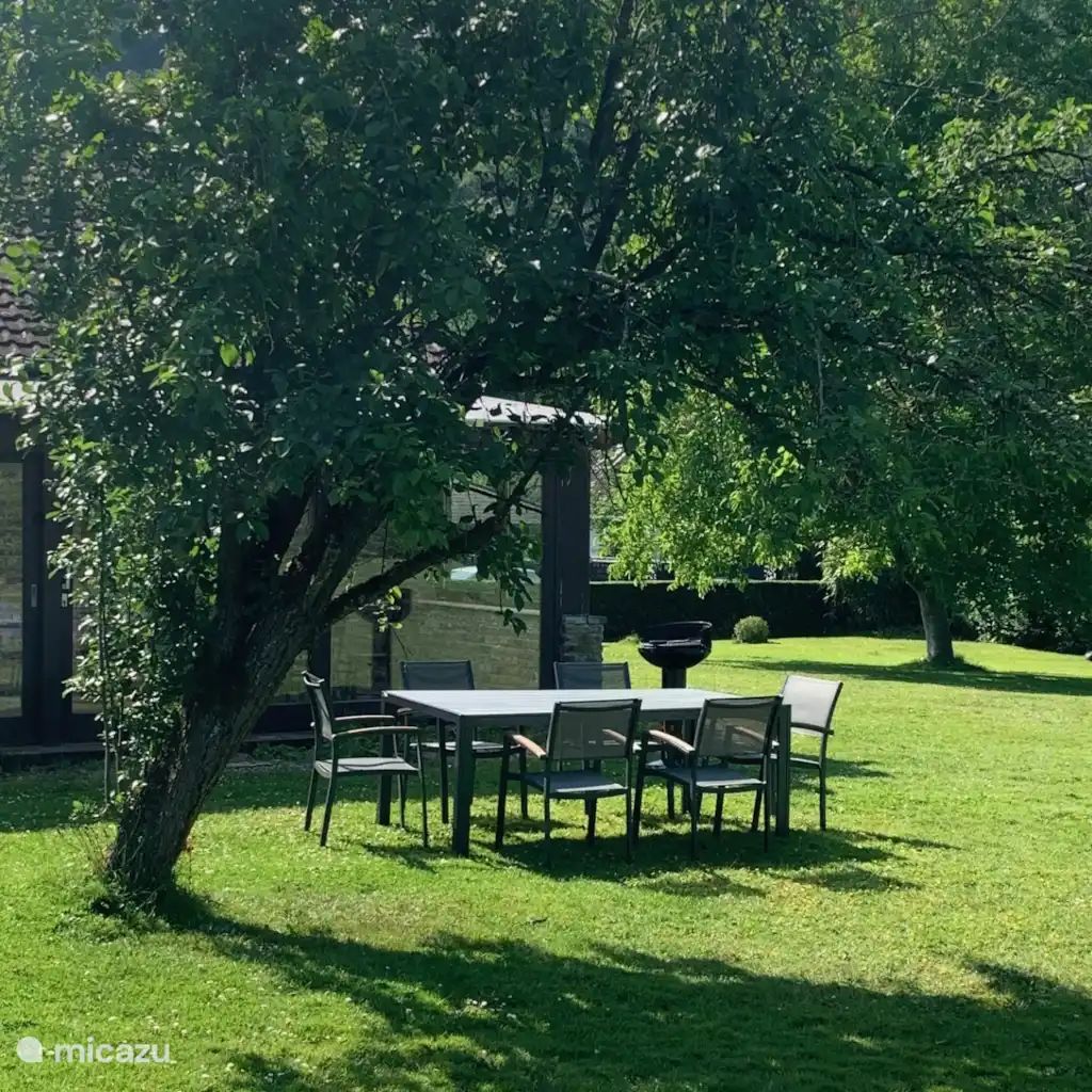 Entspannen im Garten der Villa La Meuse - De Maas, einem Ferienhaus in Dinant in den Ardennen, mit einer einladenden Terrasse unter einem schattenspendenden Baum.