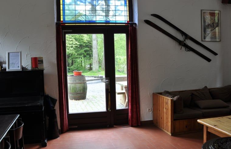 Gemuetliches Wohnzimmer in Cottage in Purnode, Ferienhaus in den Ardennen, Belgien, mit Blick auf die gruene Natur und rustikaler Einrichtung.