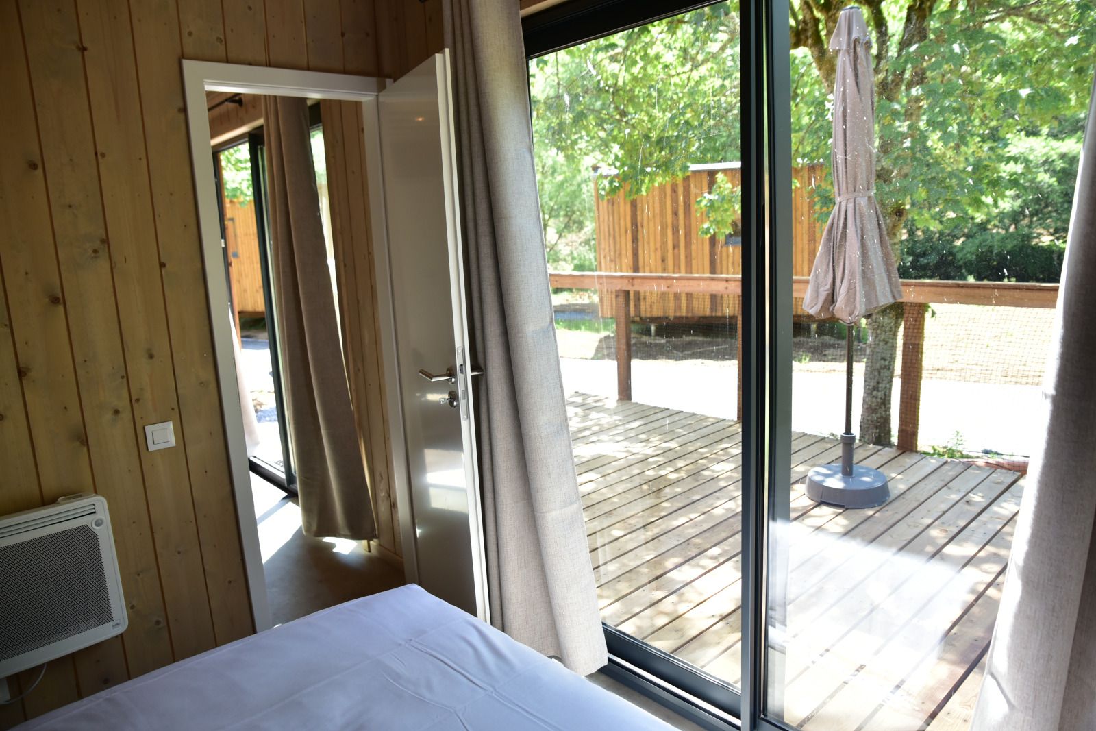 Cozy bedroom overlooking the wooden terrace of Ecolodge in Houffalize, Ardennes, perfect for nature lovers.