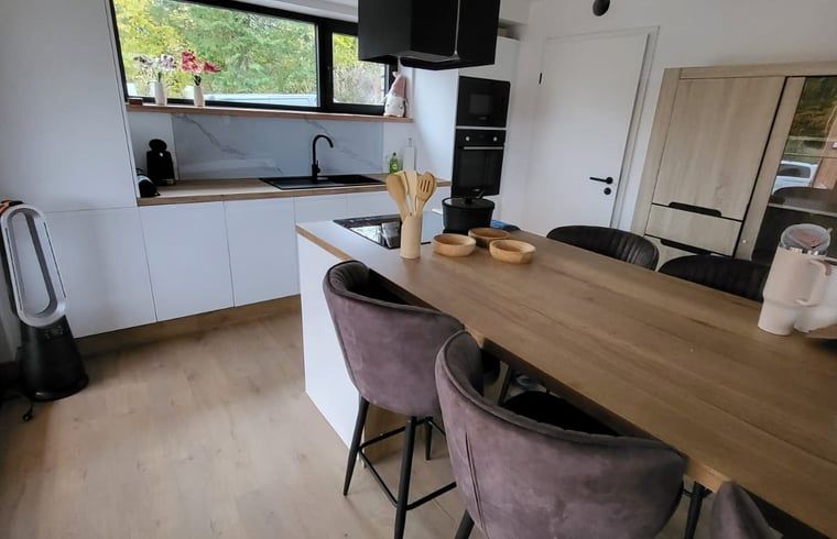 Modern kitchen of Cottage in Grandmenil, cottage in the Ardennes, Belgium, with wooden dining table and view of the green surroundings.